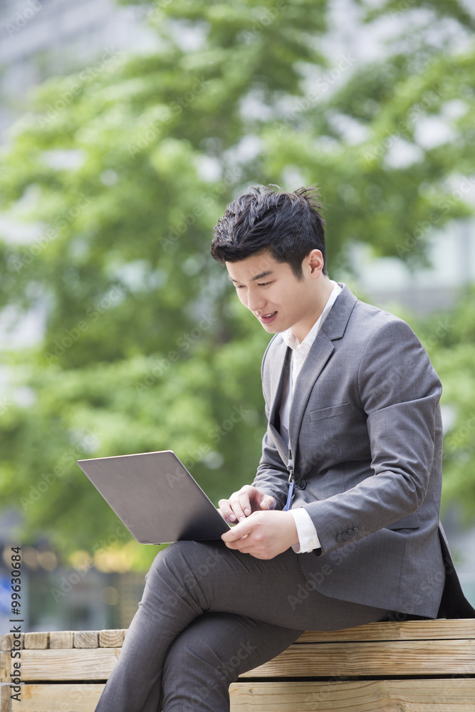 Young businessman working with laptop outdoors