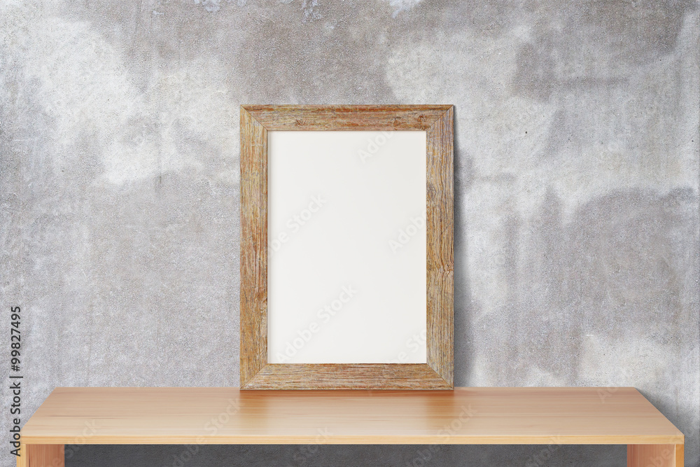 Blank wooden picture frame standing on the wooden table on a bac