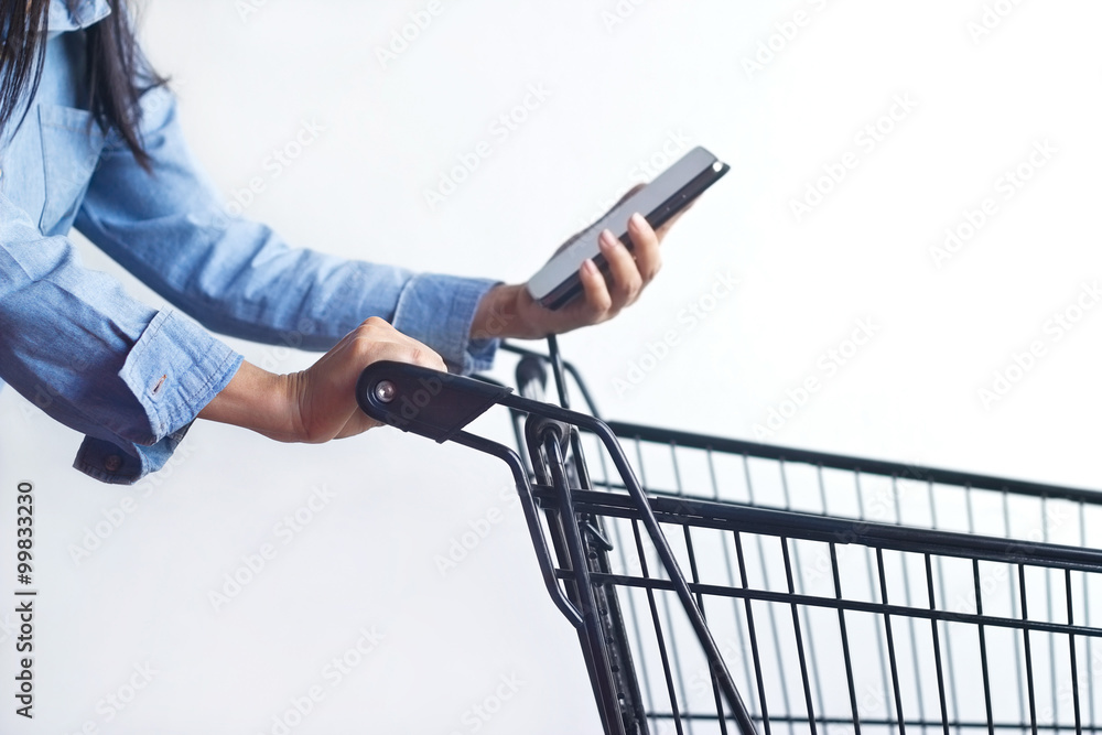 Closeup of woman with shopping cart and shopping list on smartphone in hand