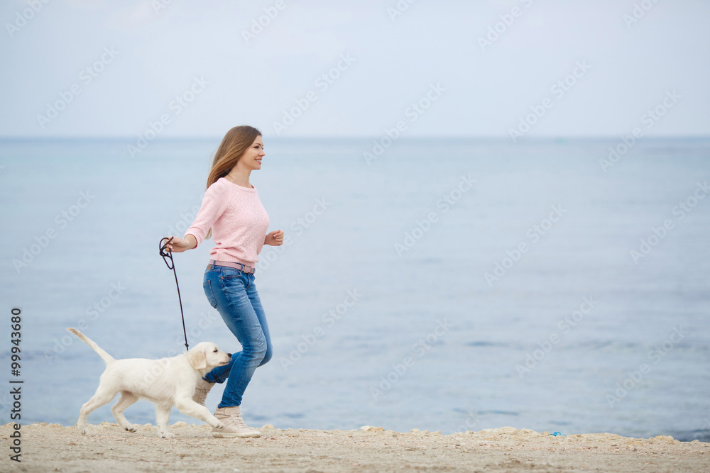 海边一名年轻女子带着一只小狗寻回犬