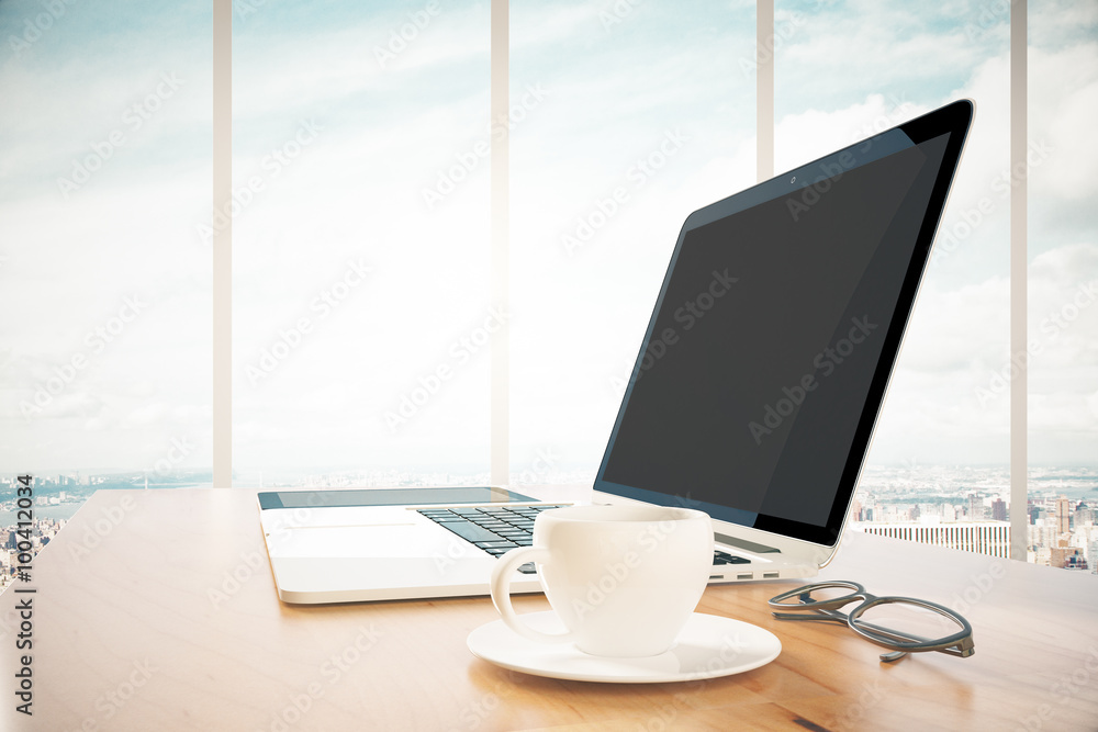 Opened laptop with cup of cooffee on wooden table in the office