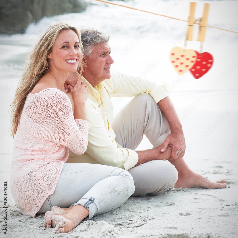 Composite image of happy couple sitting on the sand