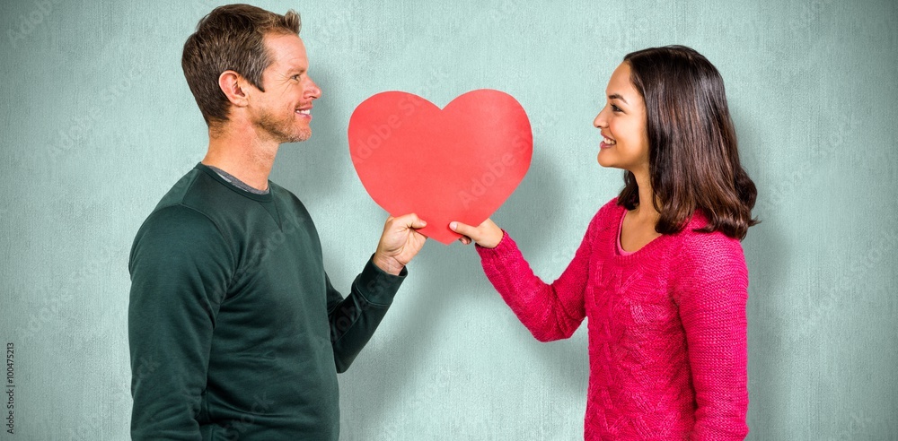 Composite image of smiling couple holding red heart shape 