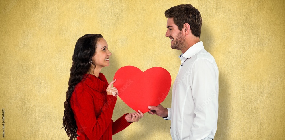 Composite image of smiling couple holding paper heart