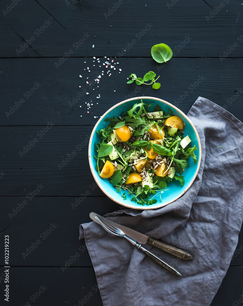 Bowl of green salad with avocado, arugula, cherry tomatoes and sunflower seeds, grilled bred slices,