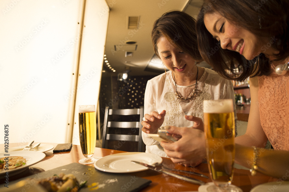 Two women looking at the mobile phone before a meal in the restaurant