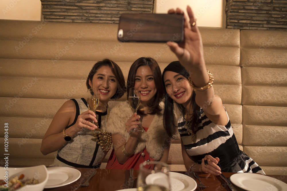 Three women are taken with smartphone while drinking champagne