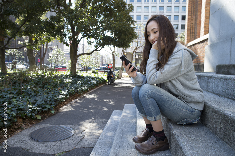 女人坐在公园的楼梯上看着智能手机