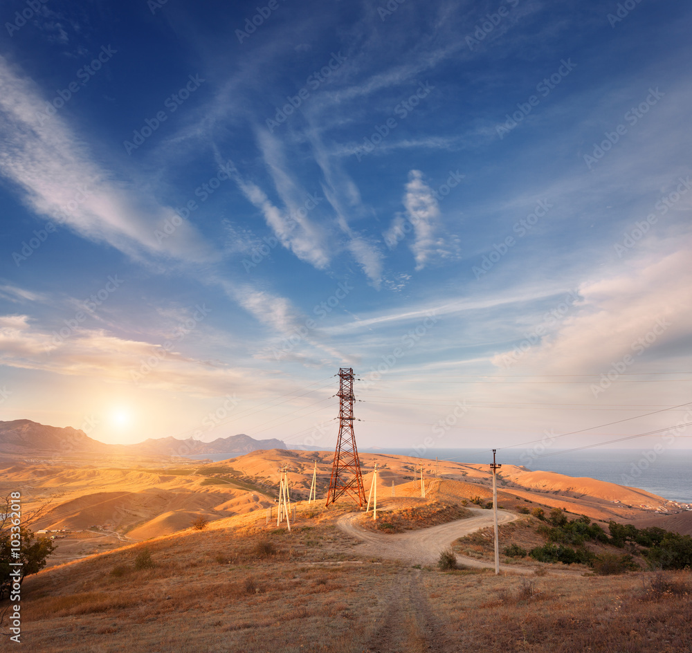 High voltage tower in mountains on the background of colorful sky at sunset.  Electricity pylon syst