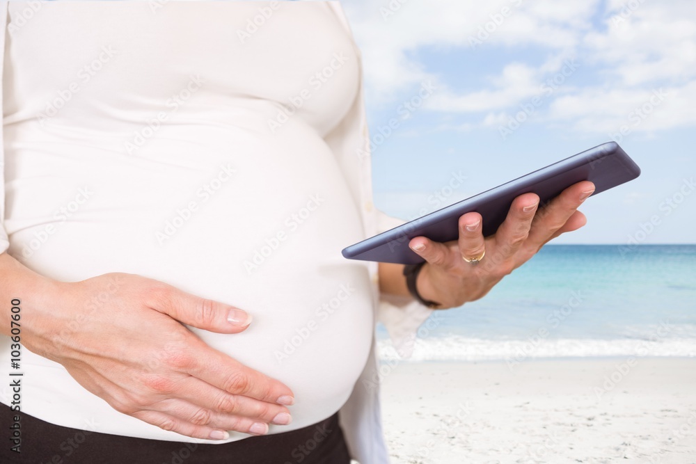 Composite image of midsection of pregnant woman using tablet