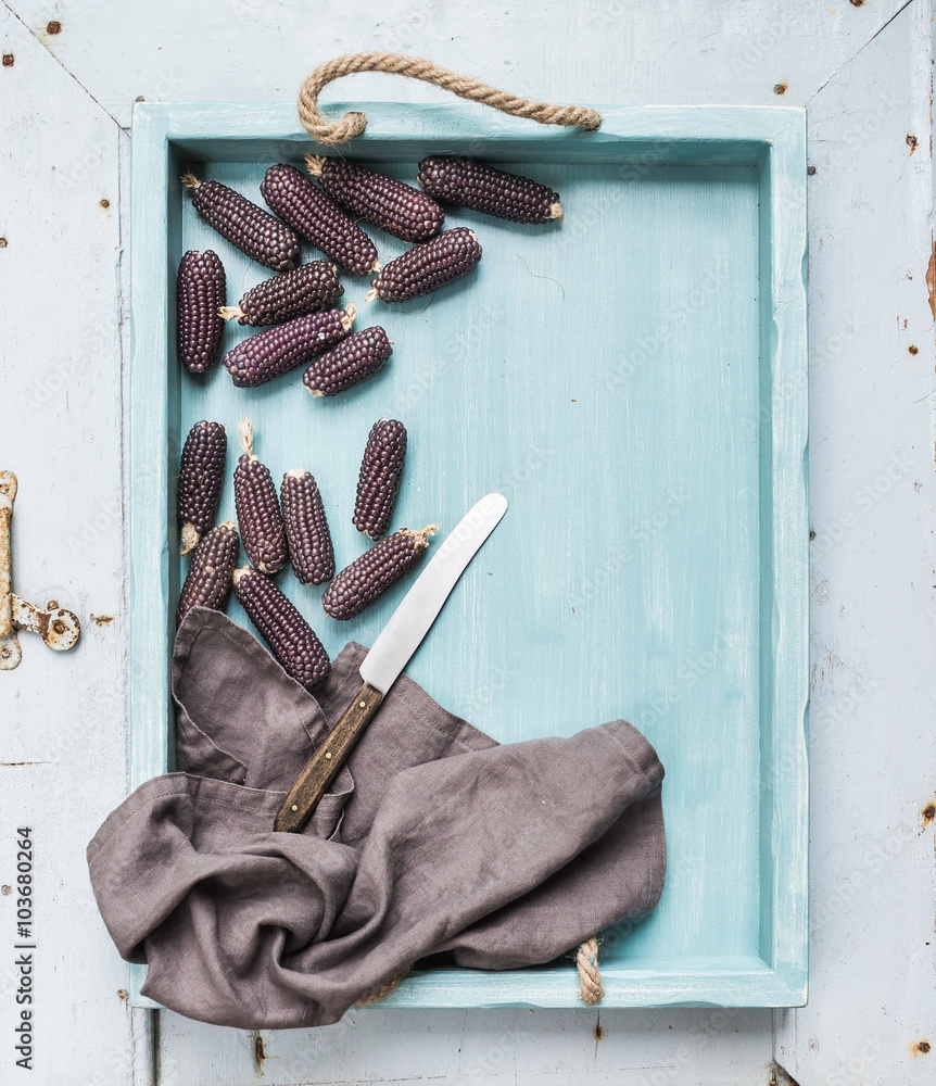 Small black corns on blue wooden tray over light rustic backdrop, top view.