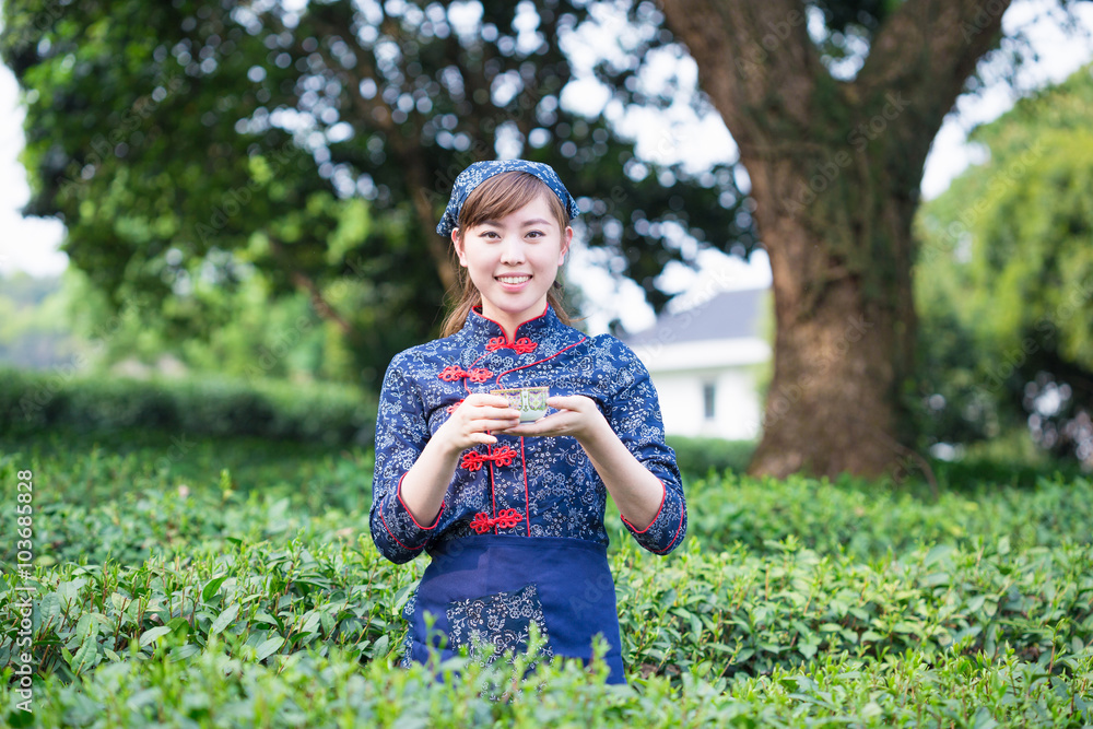 beautiful Asian girl holds cup in green tea plantation