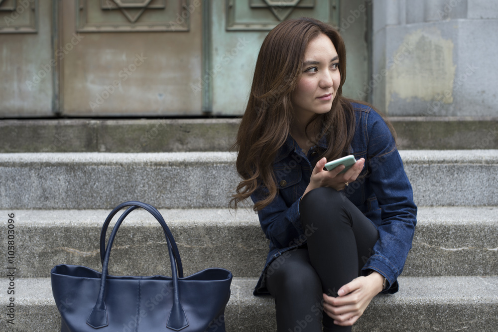 Young woman has a smart phone sitting on the outside of the stairs