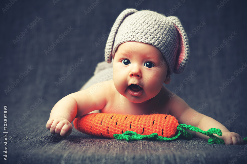 happy baby child in costume a rabbit bunny with carrot on a grey