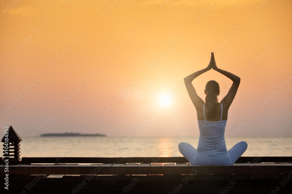 Young woman practicing yoga on the beach at sunset