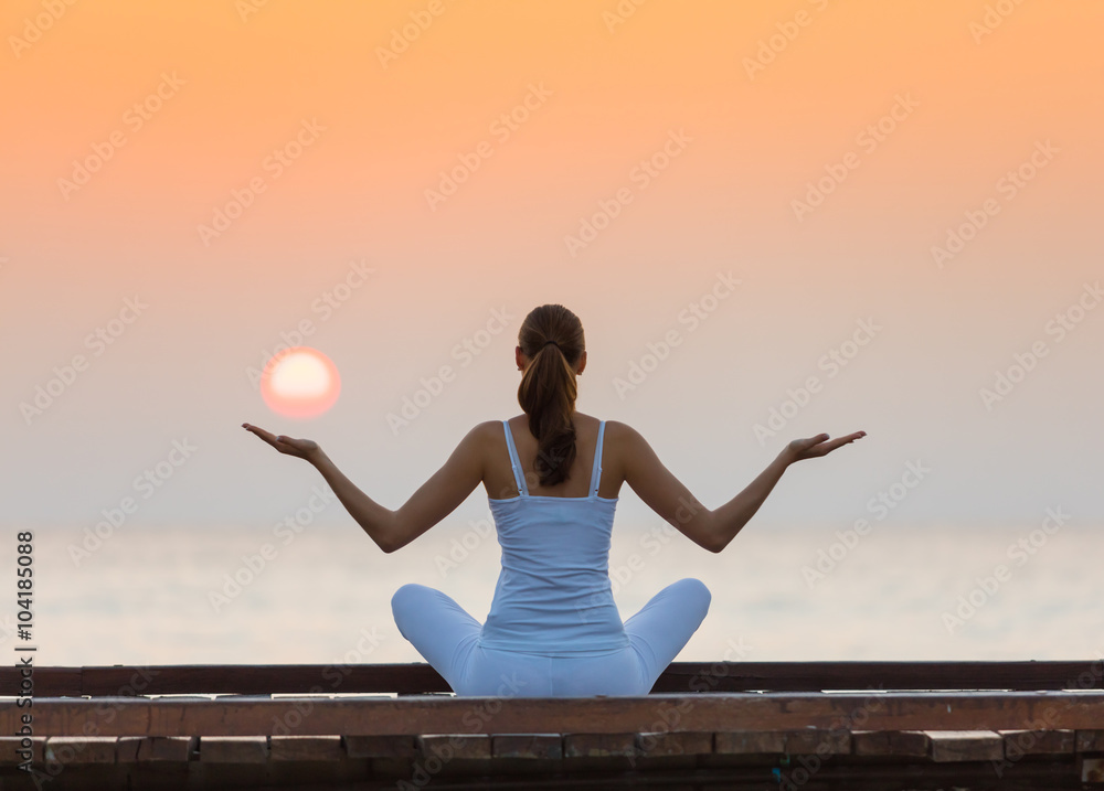 Young woman practicing yoga on the beach at sunset