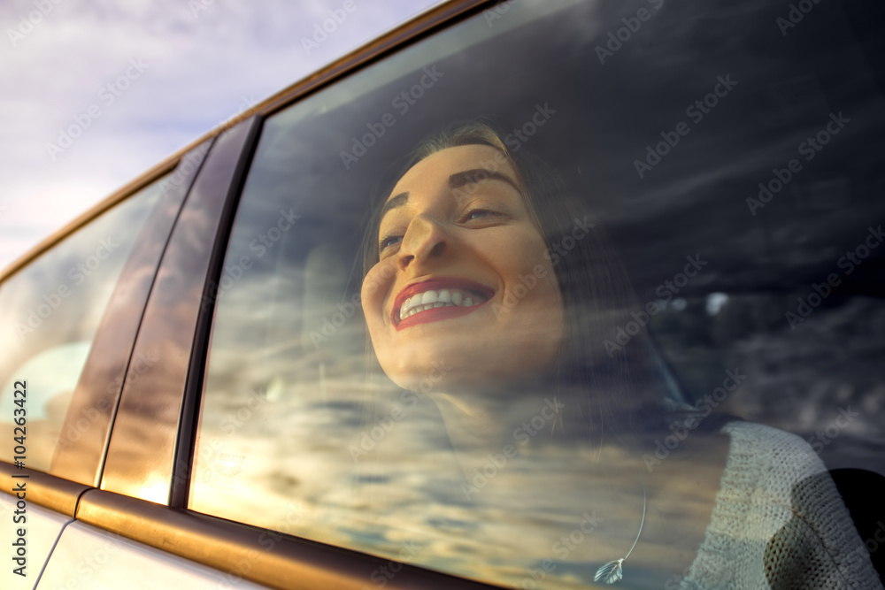 有趣漂亮的女人坐在车里透过窗户看，天空反射