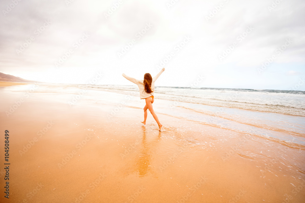 Young woman in sweater having fun enjoying beautiful sandy beach on the foggy weather on Fuerteventu