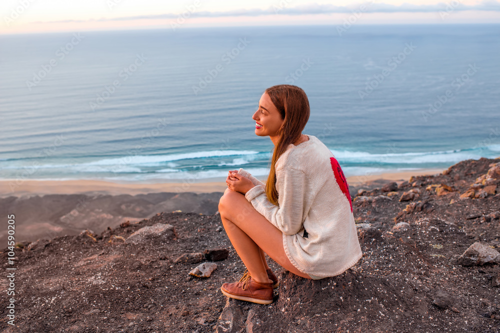 Young woman enjoying nature sitting on the mountain with ocean on background on Fuerteventura island