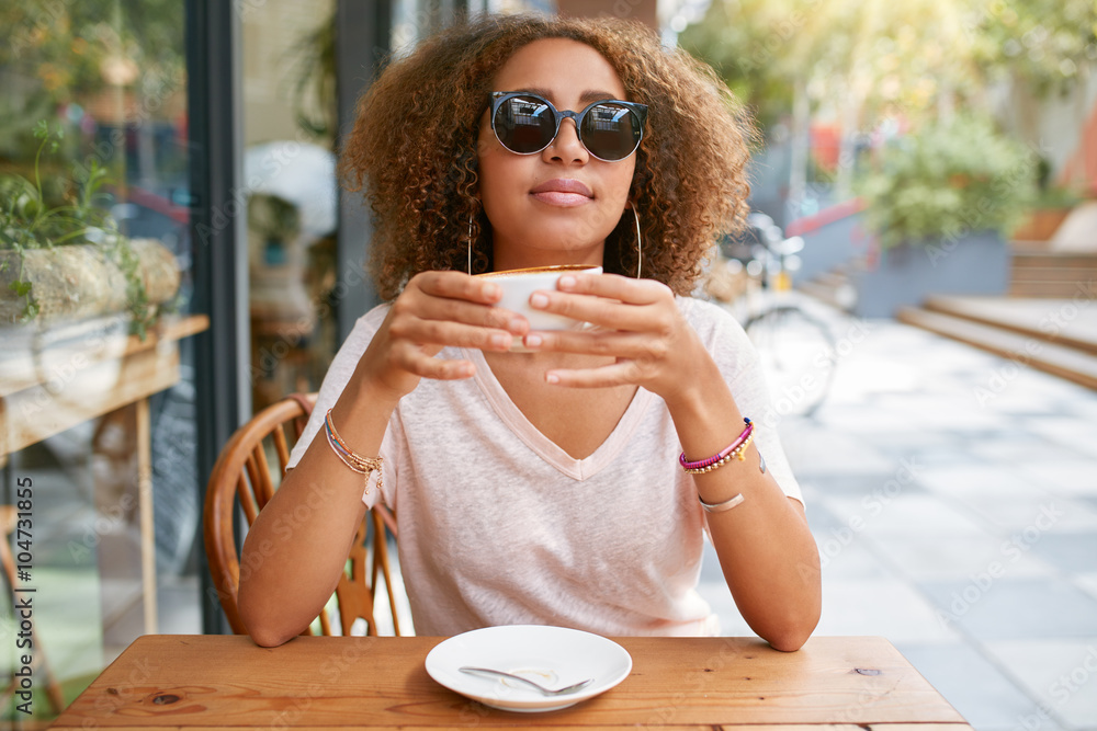 Pretty young woman drinking coffee at sidewalk cafe