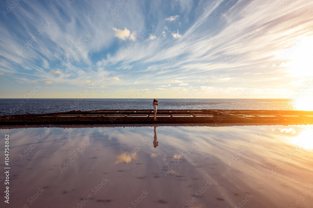 Volcanic pool with woman standing on the salt manufaturing with pink salt water and reflection on La