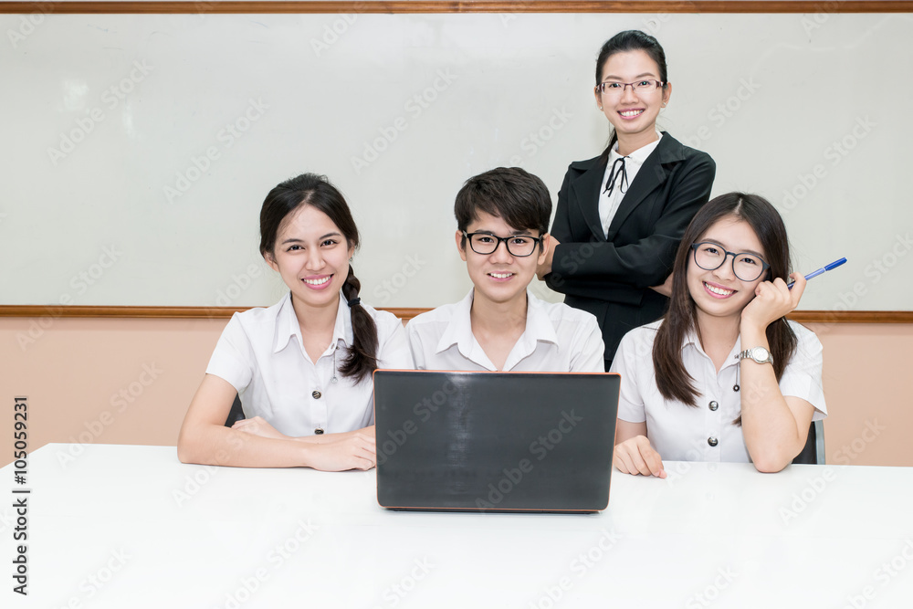 Asian teacher assisting student using laptop at desk in classroo