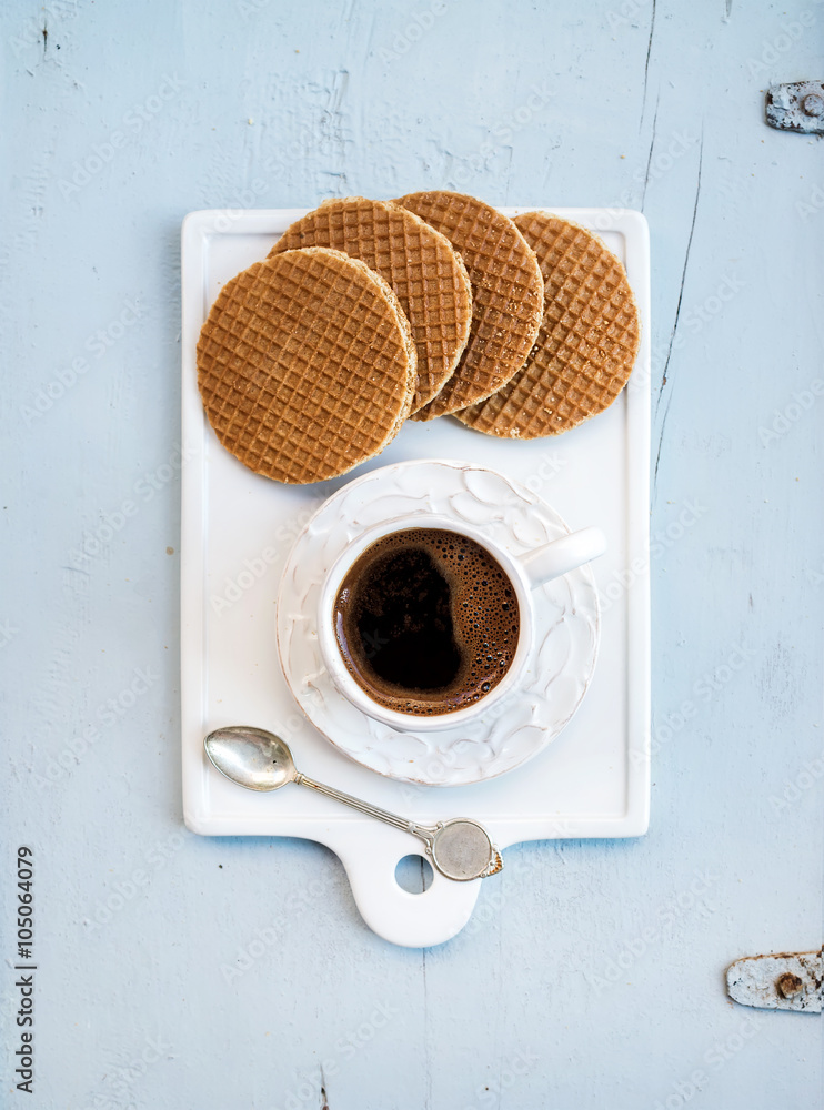 淡蓝色wo上的白色陶瓷服务板上的荷兰焦糖色stroopwafels和一杯黑咖啡