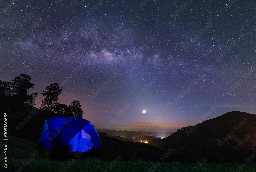 A camping tent glows under a night sky full of stars. Outdoor Camping adventure.