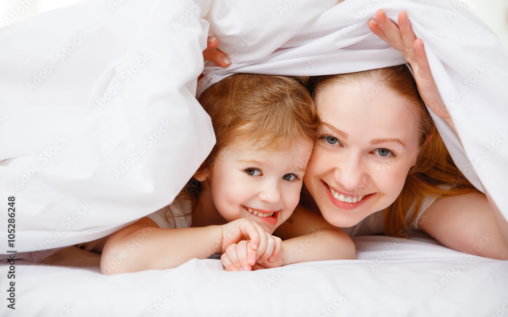 happy family mother and child playing and laughing in bed