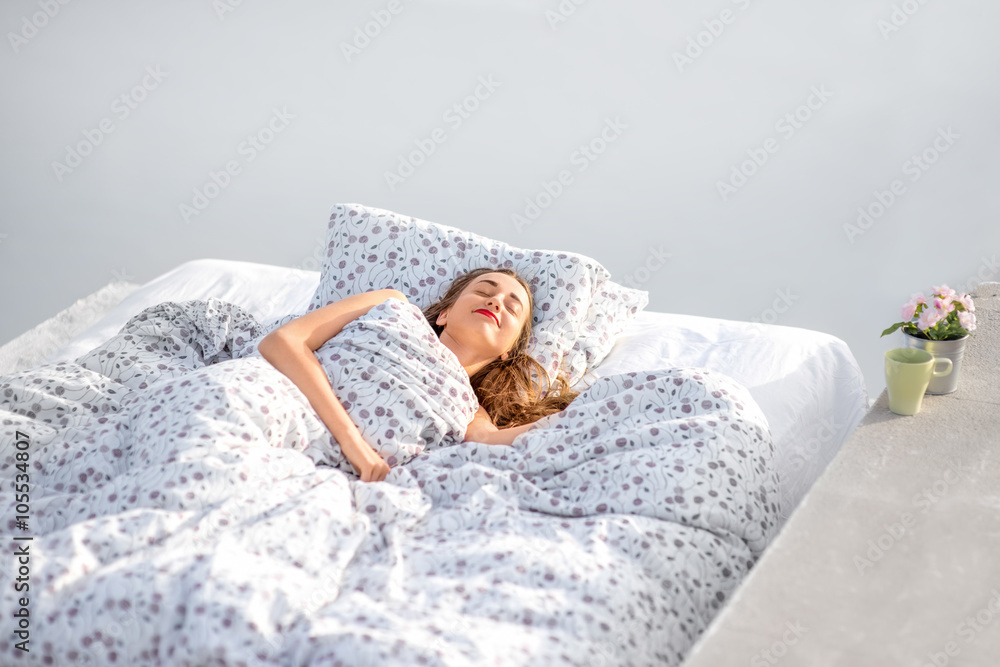 Young and cute woman sleeping on the bed outdoors on the white wall background