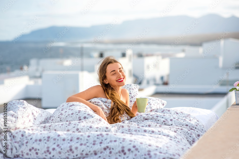 年轻可爱的女人拿着茶杯躺在屋顶的床上，白色的房子和山脉o