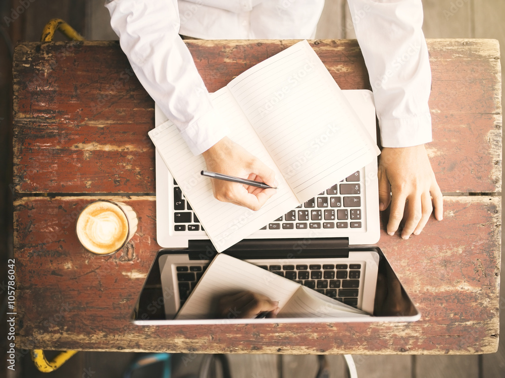 Girl writes in a notebook on a wooden desk with a cup of coffee