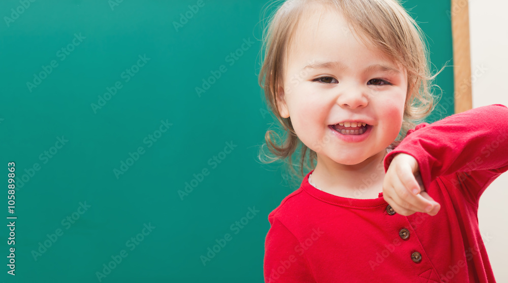 Happy toddler girl smiling in front of a chalkboard