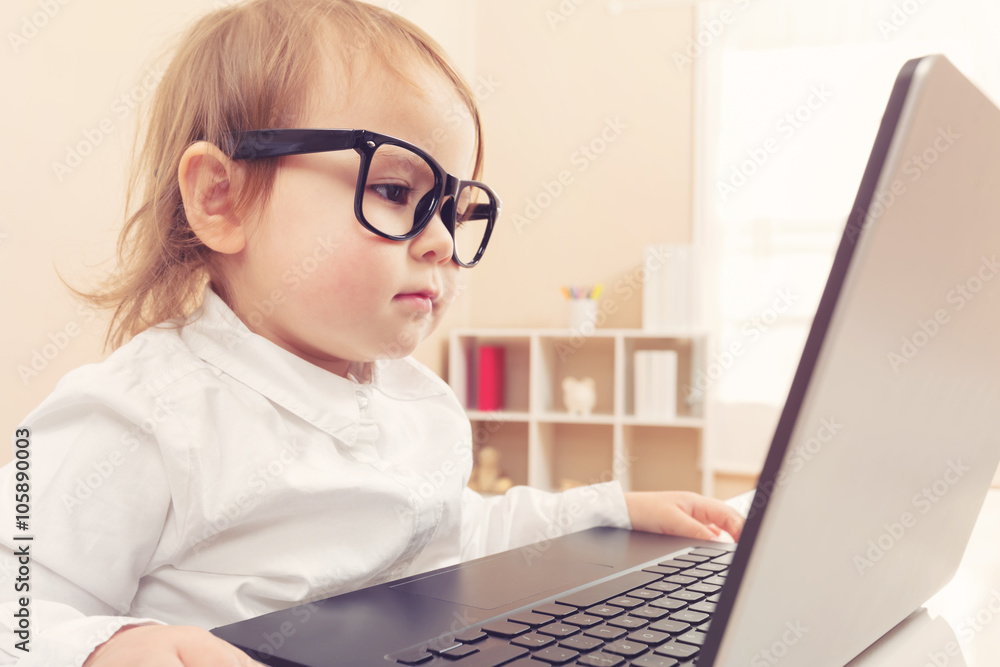 Smart toddler girl wearing big glasses using her laptop