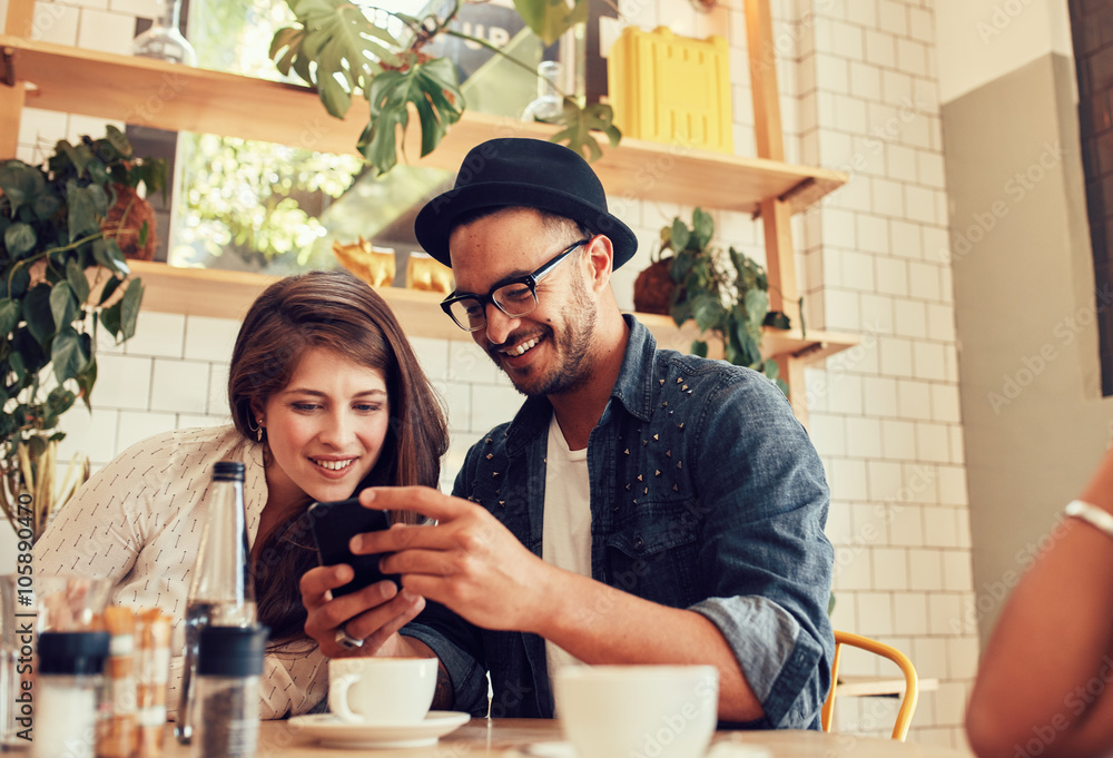 Friends looking at mobile phone while sitting in cafe