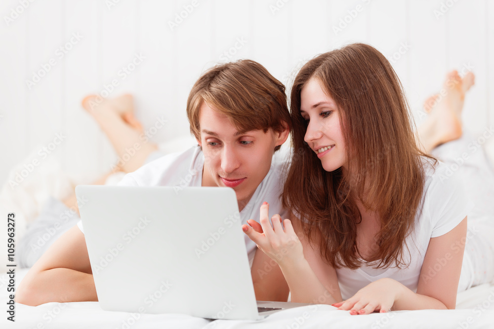 happy couple with laptop on internet in bed