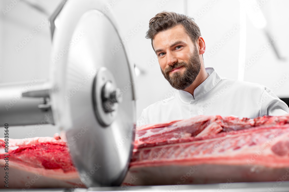 Handsome butcher cutting pork carcasse with big electric saw at the meat manufacturing