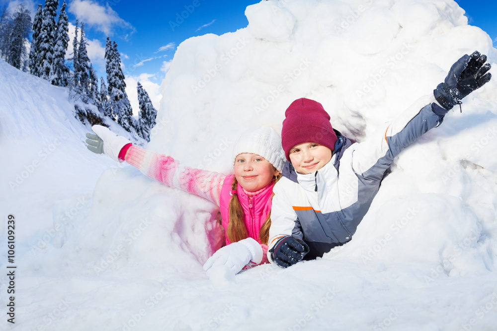 Boy and girl flourish their arms from a snow hole