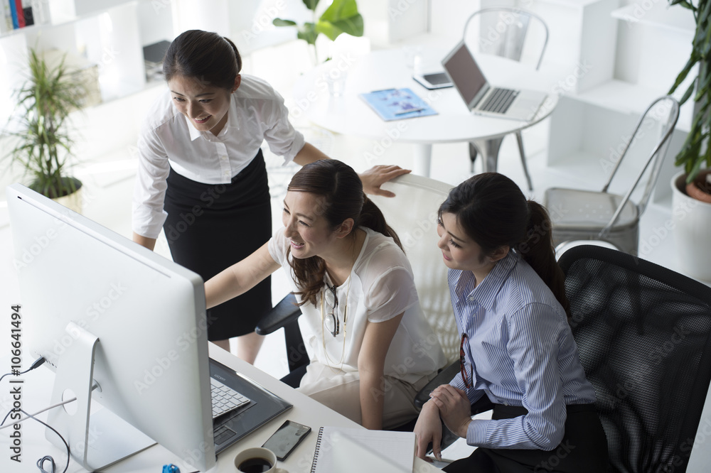 Three women are looking at the screen of a personal computer together