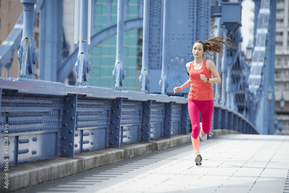 Young woman is running wearing sportswear on the bridge