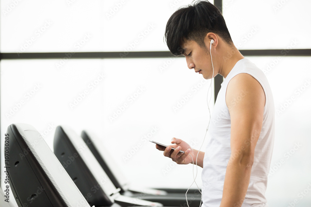 young handsome asian man using smartphone in modern gym