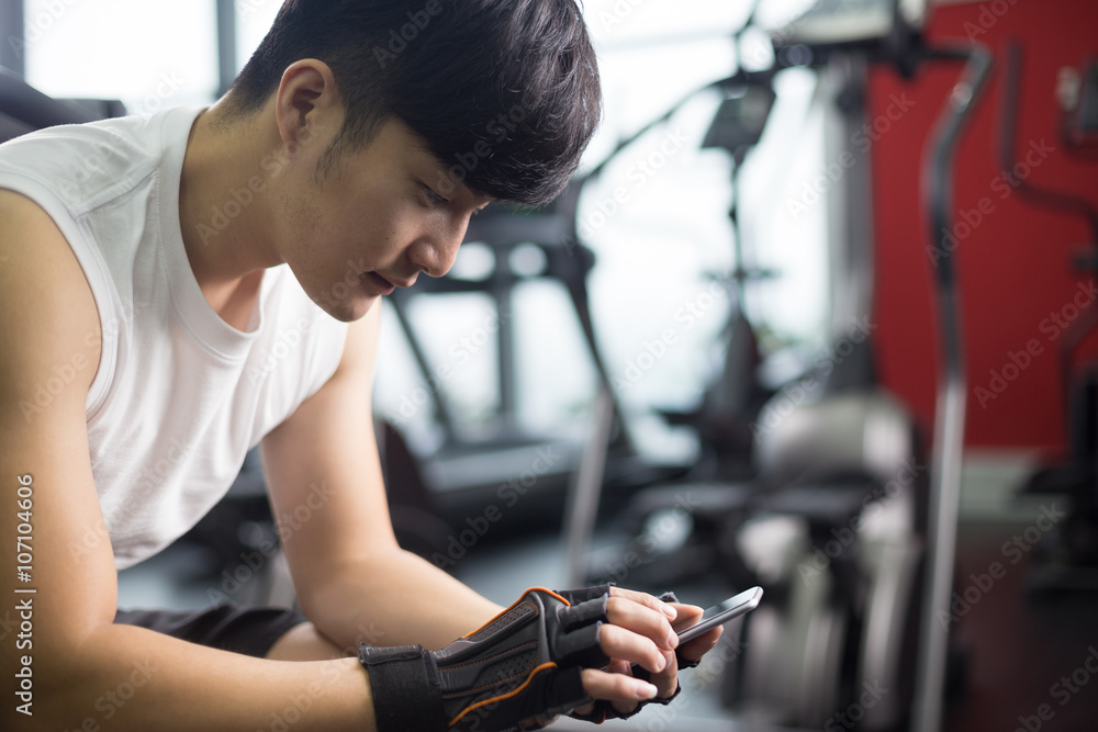 young handsome asian man using smart phone in modern gym