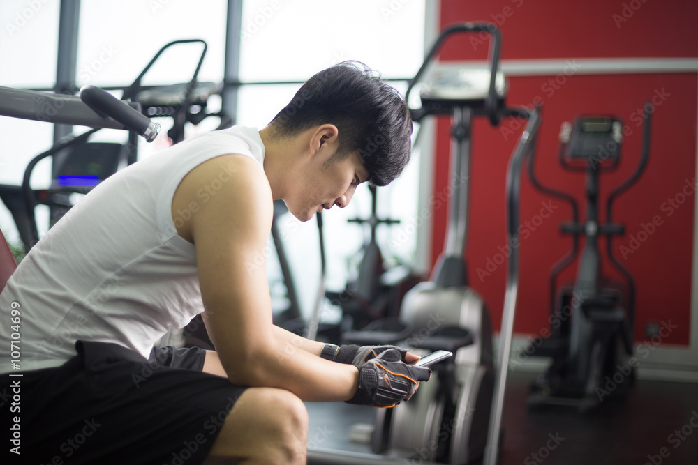 young handsome asian man using smart phone in modern gym