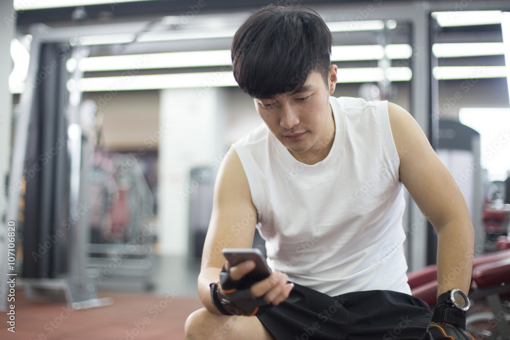 young handsome asian man using smart phone in modern gym