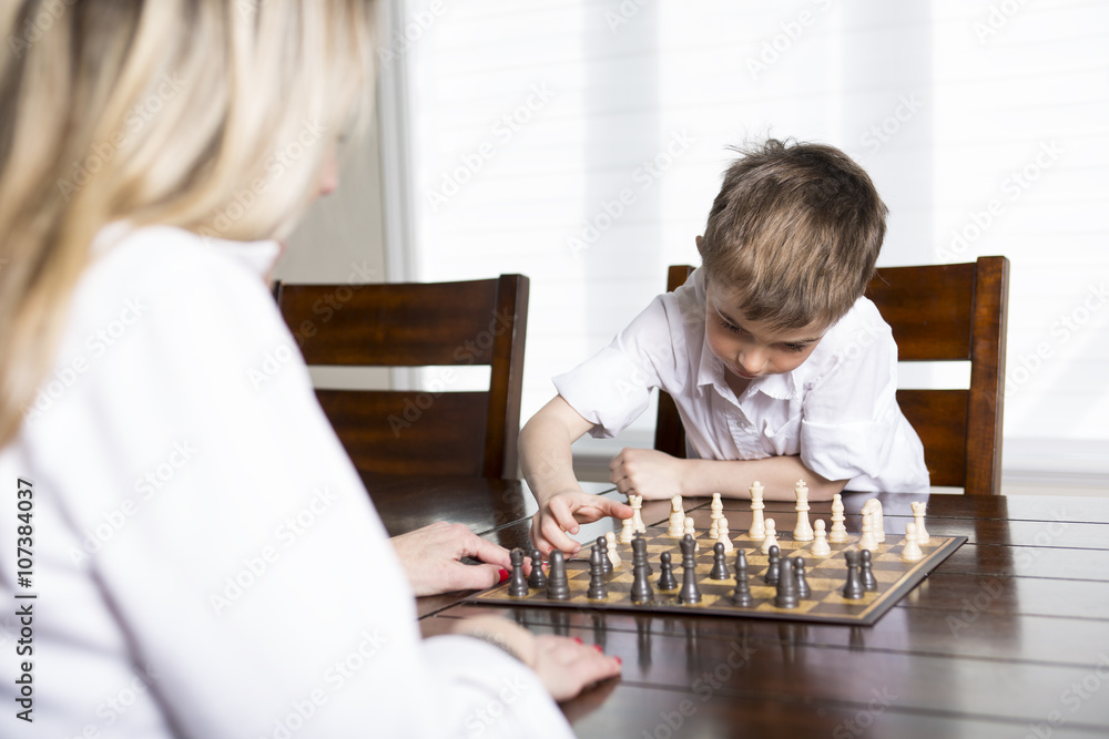 boy playing chess at home with mother