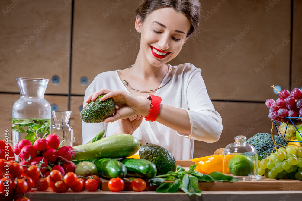 年轻漂亮的女人坐在装满水果和蔬菜的桌子旁看智能手表