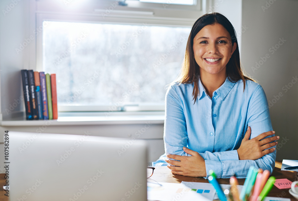 Confident grinning woman at desk behind laptop