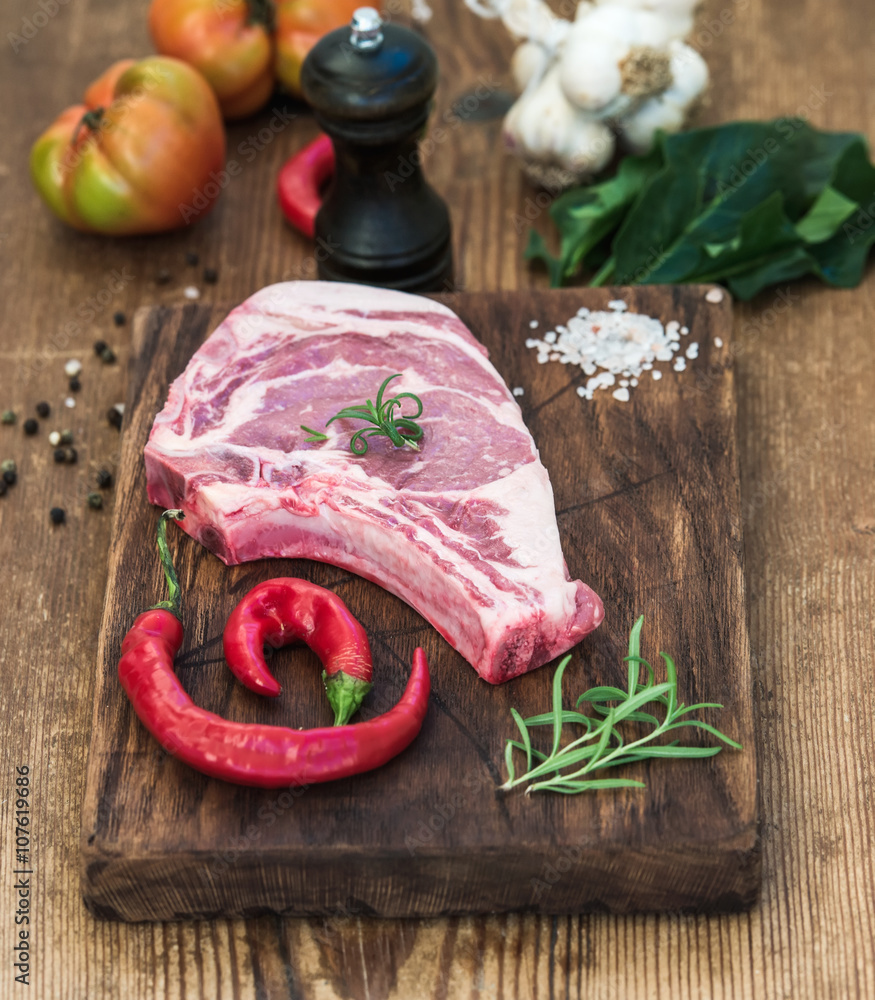 Raw fresh meat ribeye steak with salt, chili pepper, rosemary, tomatoes, garlic and spinach on rusti