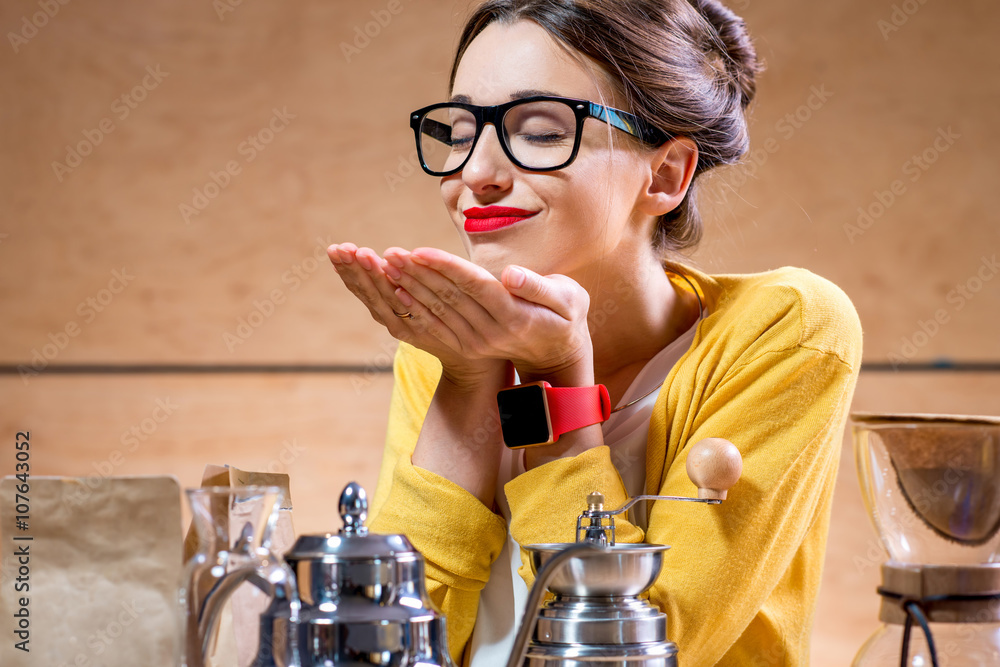 Young and pretty woman smelling coffee beans sitting at the wooden table with various stuff for alte