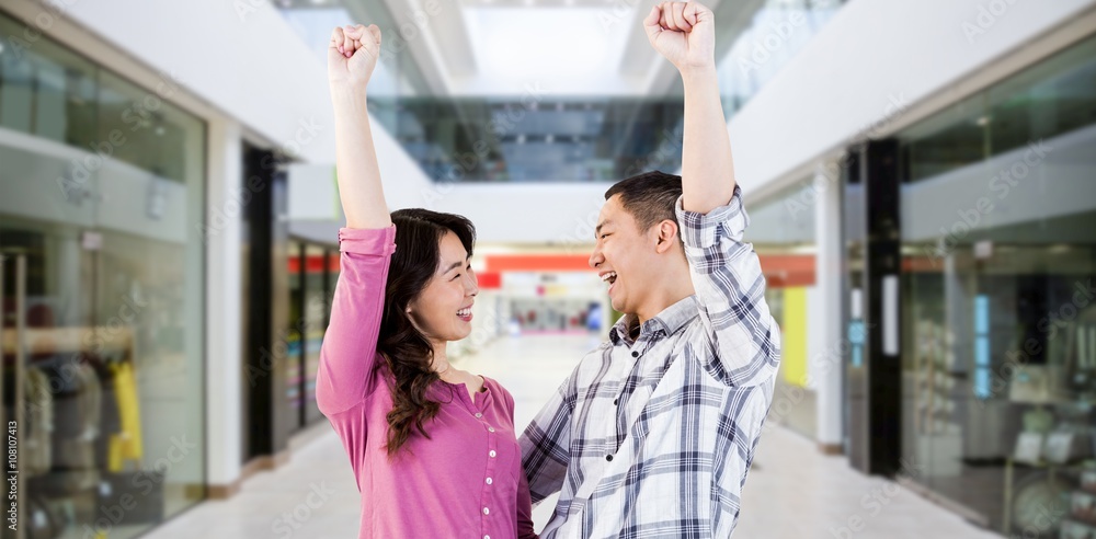 Composite image of cheerful young couple with hands raised